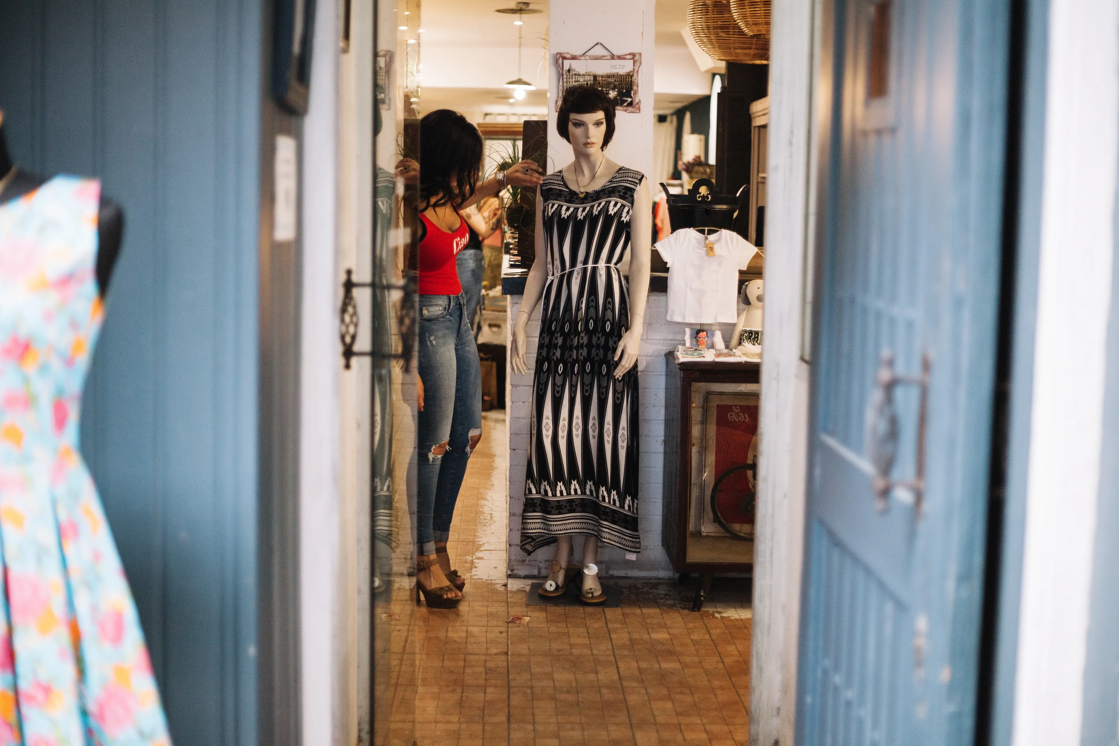 Mannequin in a boutique, framed by open blue doors, with someone adjusting its dress.