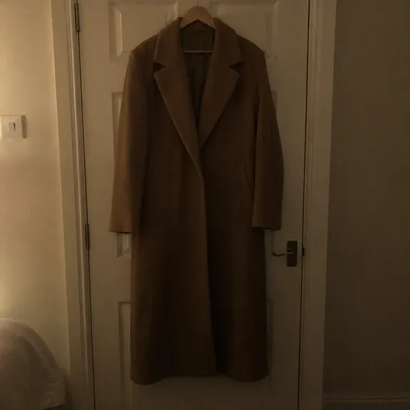 Seller photo of a camel wool coat on a bedroom door under a dim ceiling light, before relighting