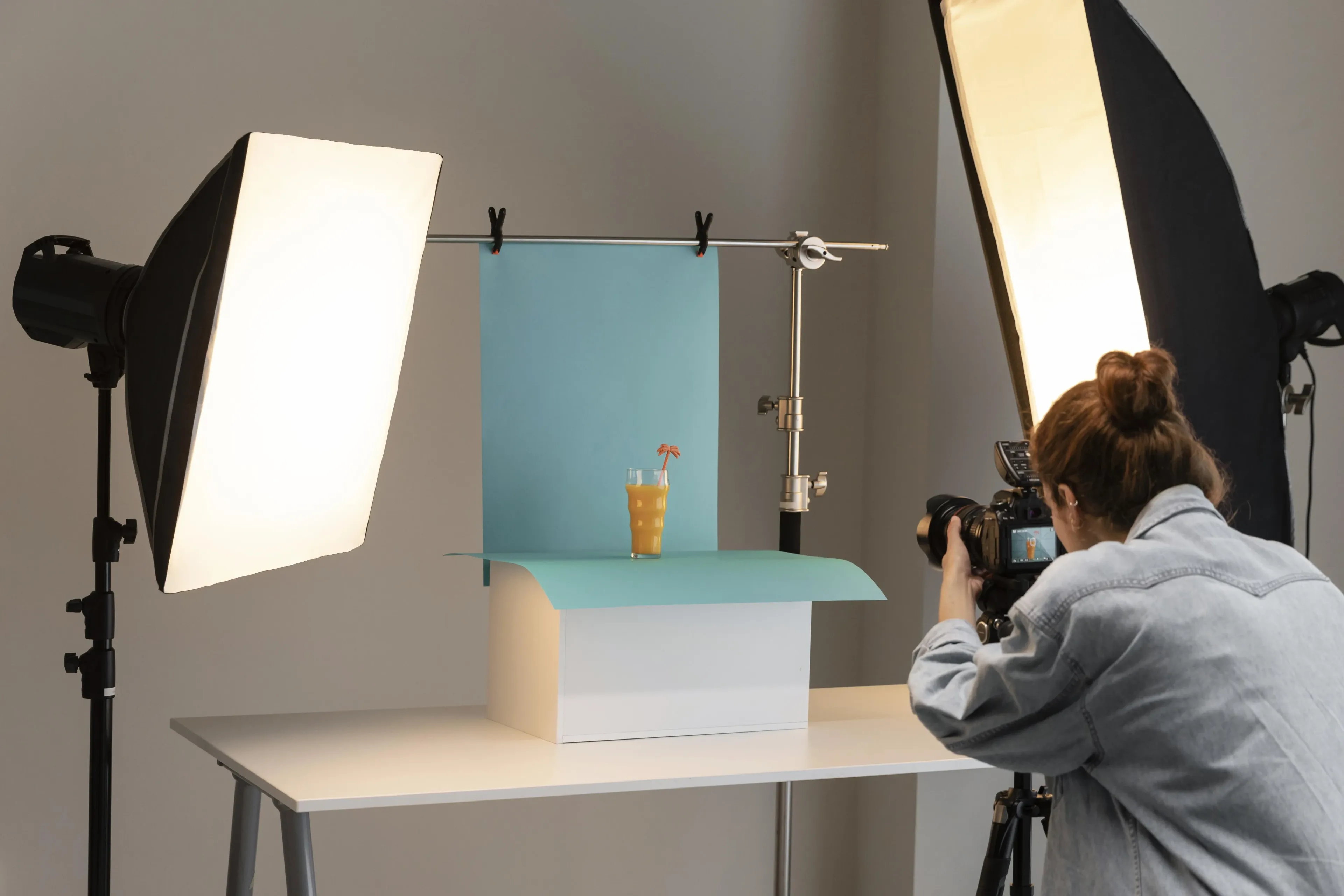 Photographer in a studio captures a drink setup with soft-box lighting and a blue backdrop.